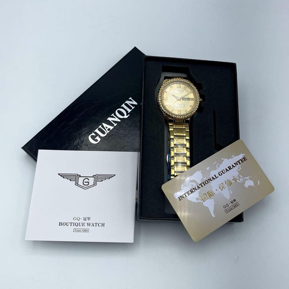 Gold watch in a black box with 'GUANQIN' branding on a light gray background