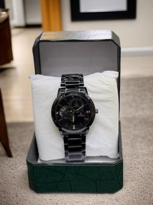 Black wristwatch in a green display box on a carpeted floor.