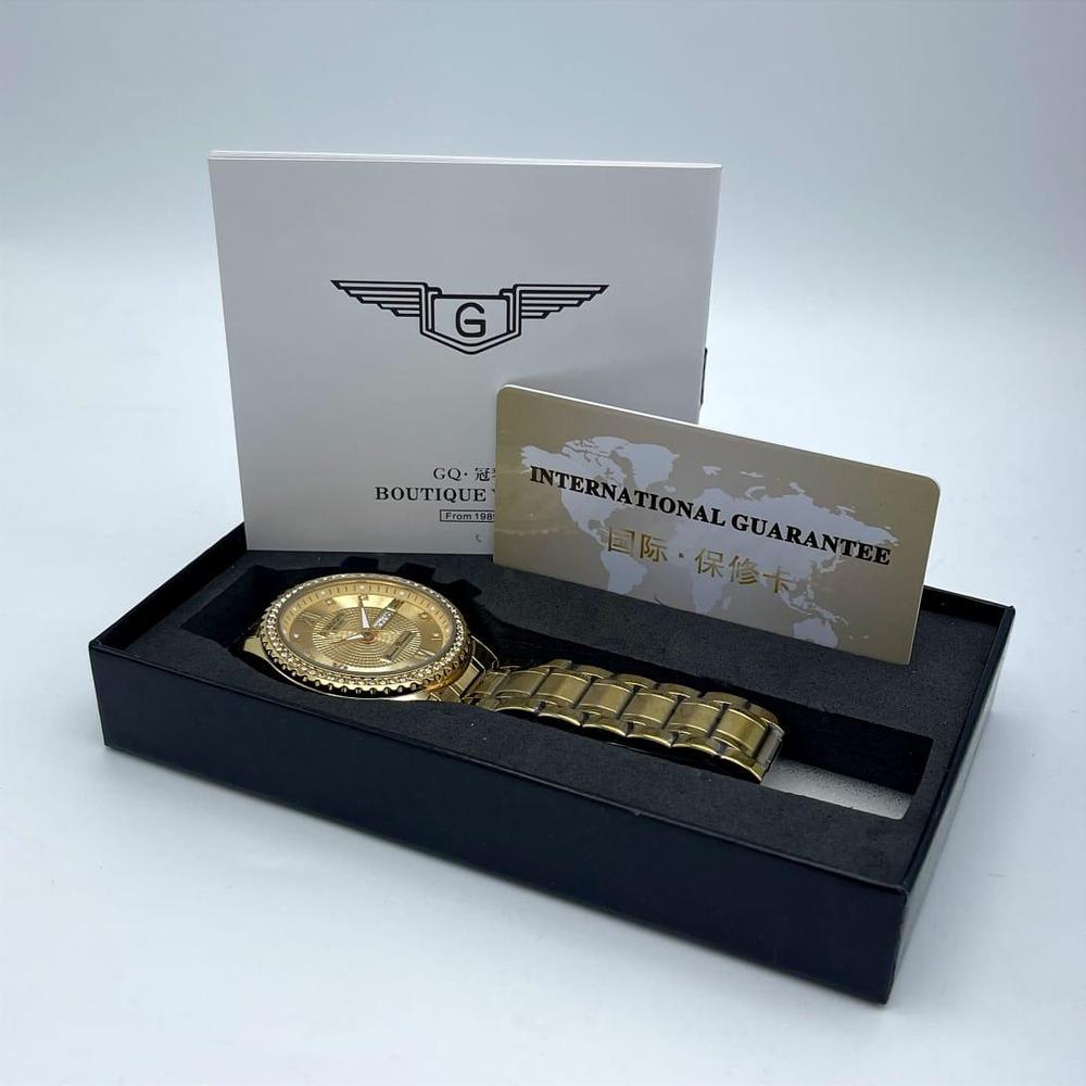 Gold watch in a black box with a white card and gold card on a light gray background