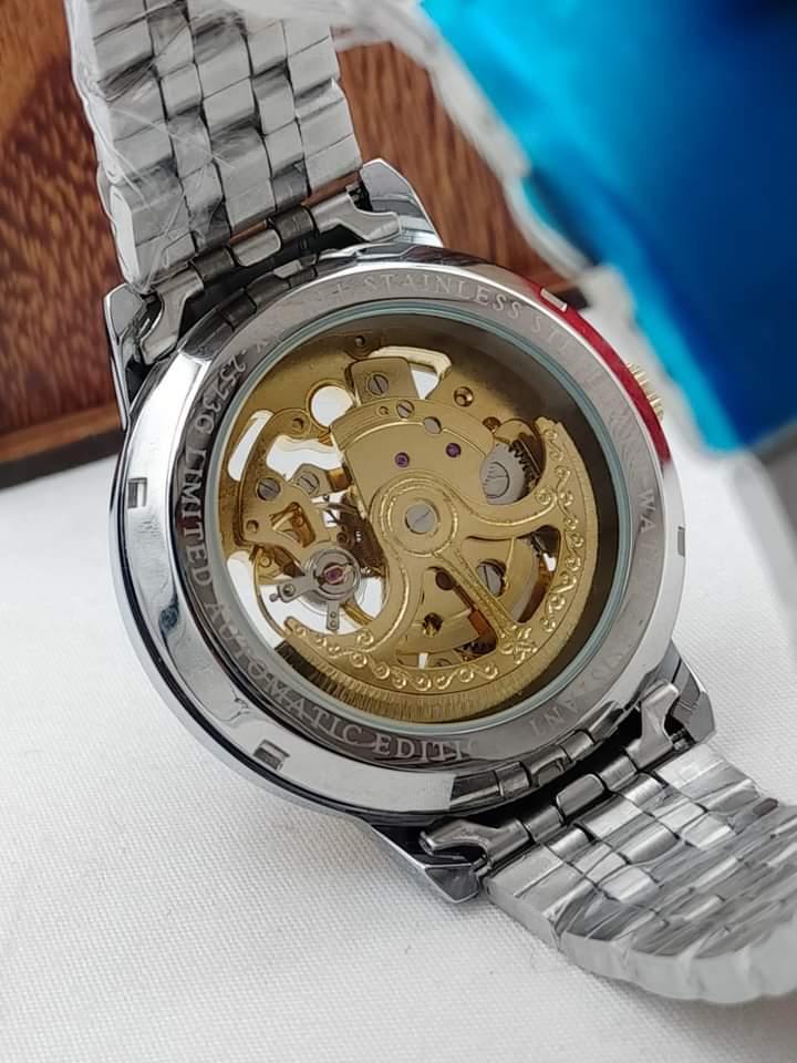 Close-up of a silver watch with a gold mechanical movement on a white surface.